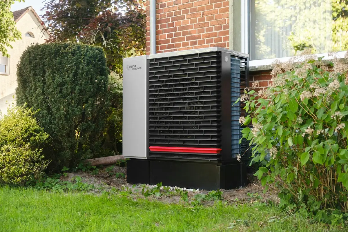 Outdoor heat pump unit on a stand next to a brick house